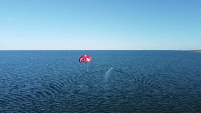 Parachuting by boat, extreme tourist entertainment, recreation and leisure at sea, aerial view. Beautiful landscape of the blue sea that merges with the horizon of the blue sky