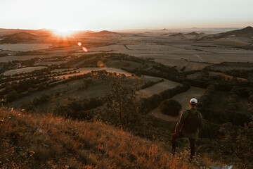 Young man with backpack walking down from hill and looking to Czech ore mountain valley at sunrise. Czech toned landscape