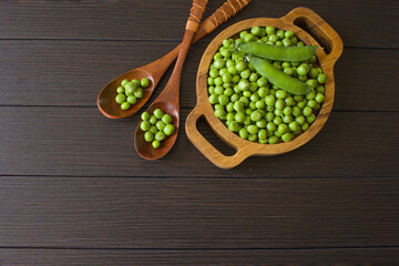 peeled green peas in a wooden plate and spoons top view. background with green sweet peas. green peas are cleaned and in the pod.