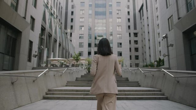 Shot back woman wearing formal suit walking hold coffee and tablet computer look around outside business cellphone city smartphone slow motion
