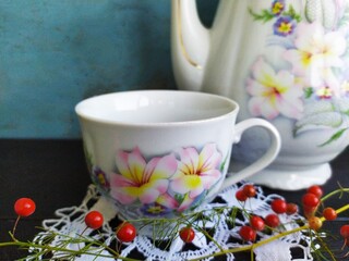 Delicate white with flowers to a porcelain teapot and cup on a lace napkin on a black wooden table