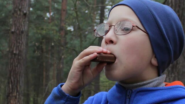 boy eats chocolate in glasses,in the forest in autumn a boy eats chocolate