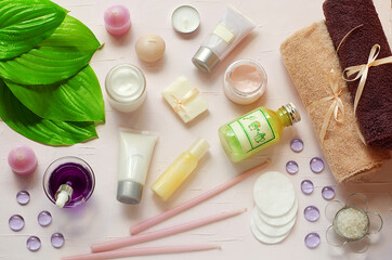 Obraz na płótnie Canvas Green fresh leaves on the background of organic cosmetics. Towels, cotton pads, pink cream, green gel, candle soap. Natural cosmetics. SPA. Aromatherapy.Flat view