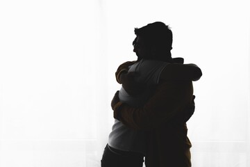 Silhouette of gay couple embracing over white background