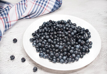 Ripe blueberries lie on a white plate on a light background.Summer vitamins. Horizontal arrangement. Place for copy space