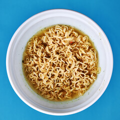 instant noodles at white bowl over blue background with copy space. fast food concept. flat lay