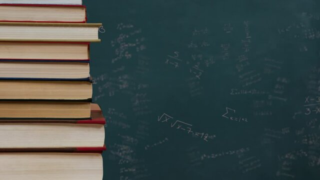 Stack of books against mathematical equations on black board