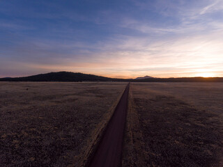 Obraz na płótnie Canvas Aerial of a gravel country road leading across a prairie into the sunset