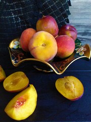 Food still life with fruits ripe peach red plums on a green bowl on the black wooden table