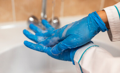female doctor in a white coat and blue medical gloves lathers her hands with soap close-up. One way...