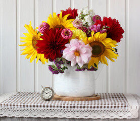 Fototapeta na wymiar bouquet of sunflowers and dahlias in a teapot and an alarm clock.
