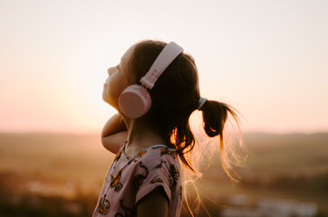 Fototapeta premium Side view close up portrait of a child with pink headphones listening to music looking up