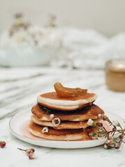 Delicious and hearty breakfast. Pancakes are stacked on top of each other with white flowers between them, pancakes topped with apricot jam. The jam is dripping over the pancakes. Flowers in food.