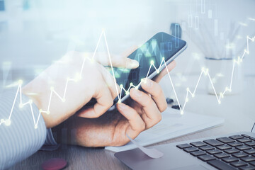 Double exposure of man's hands holding and using a digital device and forex graph drawing. Financial market concept.
