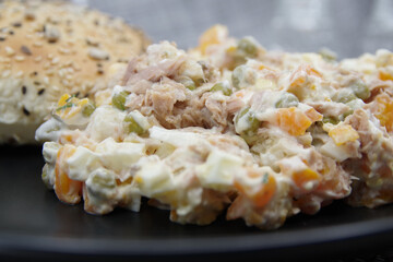 Tuna salad in black plate. Ingredients: tuna, carrots, eggs, onion, canned peas, croutons, mayonnaise