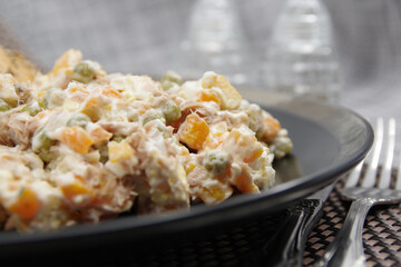 Tuna salad in black plate. Ingredients: tuna, carrots, eggs, onion, canned peas, croutons, mayonnaise