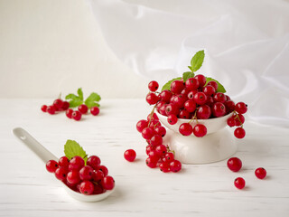 Fresh red currant berries lie in a Cup and spoon on a white background. soft focus