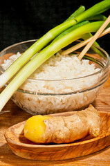 top view, close up, of elements of fried rice dinner, with green onions, chop sticks, glass bowel of steamed rice and wood bowel of fresh ginger on a wood cutting board 