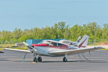 front view, close distance of a single, prop, airplane secured with tie downs, in parking tarmac, of  a tropical airport