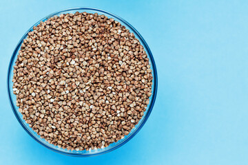 Buckwheat in a glass bowl on a blue background. Dry buckwheat background. Buckwheat texture. A product of proper nutrition. Buckwheat grain background texture. Vegetarian food.