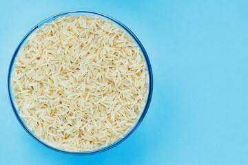 Basmati rice groats in a glass bowl on a blue background. Dry basmati rice background. Basmati rice texture. A product of proper nutrition. Basmati rice grain background texture.Vegetarian food.