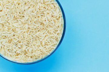 Basmati rice groats in a glass bowl on a blue background. Dry basmati rice background. Basmati rice texture. A product of proper nutrition. Basmati rice grain background texture.Vegetarian food.