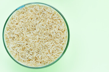 Basmati rice groats in a glass bowl on a light green background. Dry basmati rice background. Basmati rice texture. A product of proper nutrition. Basmati rice grain background texture.Vegetarian food