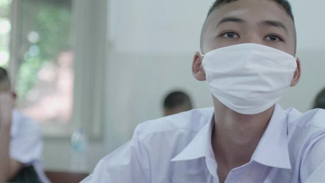 Slow motion of a male Asian high school student in white uniform and wearing a white mask is studying in classroom during the Coronavirus 2019 (Covid-19) epidemic.