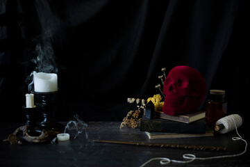 witch or wizards desk, smoking candles on library table with vintage books, magic wand and other halloween decor, and a dark background with copyspace