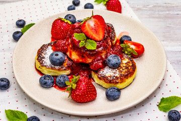 Cottage cheese pancakes with fresh berries and strawberry sauce. Healthy breakfast concept on wooden background