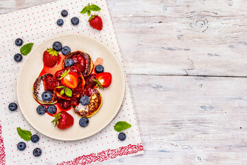 Cottage cheese pancakes with fresh berries and strawberry sauce. Healthy breakfast concept on wooden background