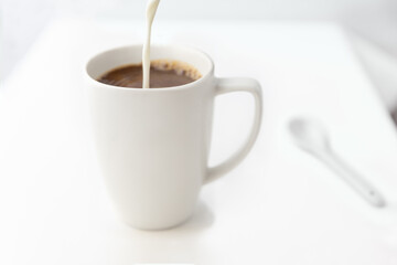 Coffee creamer being poured into a cup of coffee.