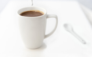Coffee creamer is dripping into a freshly poured cup of coffee.