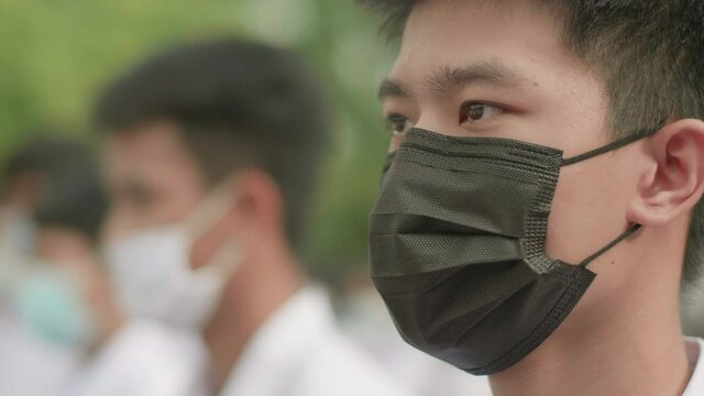 Slow motion of male Asian high school students in white uniform on the semester start wearing masks and stand in line in the morning  during the Coronavirus 2019 (Covid-19) epidemic.