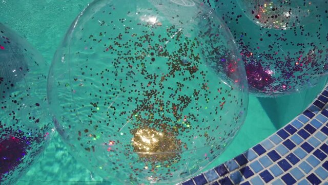 Balls with sparkles floats in the pool with blue water. Summer vacation and fun time in the swimming pool