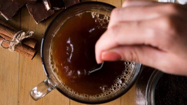 Close up of preparing hot beverage. Concept. Hand holding coffee spoon and stirring hot coffee on vintage old wooden background with cinnamon and chocolate.