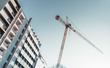 Fototapeta premium Tilted diagonal view from the ground of a high construction crane in a residential district near a dwelling house with clear blue sky in the background, a cold sunny day, Lisbon, Portugal