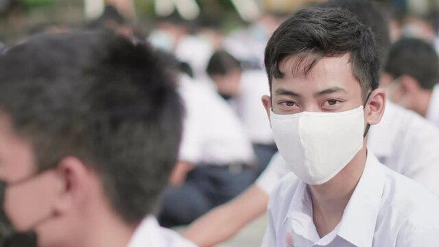 Slow motion of male Asian high school student in white uniform on the semester start wearing masks turn his face to look straight during the Coronavirus 2019 (Covid-19) epidemic.