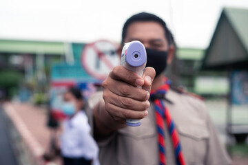 Teacher use infrared thermometer gun forehead temperature test to check student for protect virus covid-19 symptoms in the school