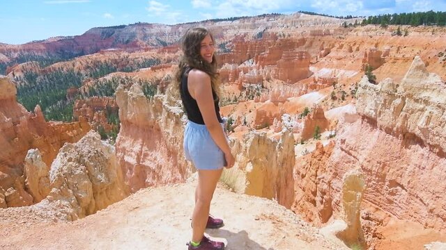 Woman person turning around looking at view happy in slow motion from overlook cliff at Bryce Canyon National Park in Utah on Queens Garden Navajo Loop hiking trail