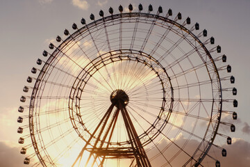 Ferris wheel spinning slowly in amusement park with sky in the background. Golden sunset in background.