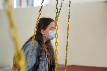 Teenager girl sitting on the swing with face protective mask. Concept social distance. Back to school in a new reality.