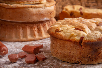 artisan breads on a wooden table dirty with flour and with ingredients olives, eggs and sausage and rosemary.