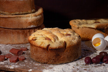 artisan breads on a wooden table dirty with flour and with ingredients olives, eggs and sausage and rosemary.