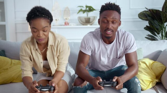 Young woman fixing problem in playstation console device. Happy african american couple starting play computer online video games with joysticks.