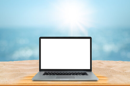 Summer Travel Trip and Work from Anywhere Concept, Business Travel Concept : Laptop with blank white screen on wooden table and blurry image of seascape in background. © Angkana