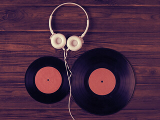 Two vinyl discs and white headphones with a wire on a wooden background.