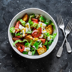 Crunchy bread, fresh tomatoes, mozzarella cheese, green salad  on a dark background, top view