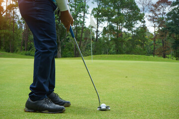 Fototapeta premium Golf player at the putting green hitting ball into a hole