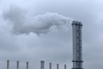 Smoke comes from industrial chimneys. The sky is covered with gray clouds. Environmental pollution.